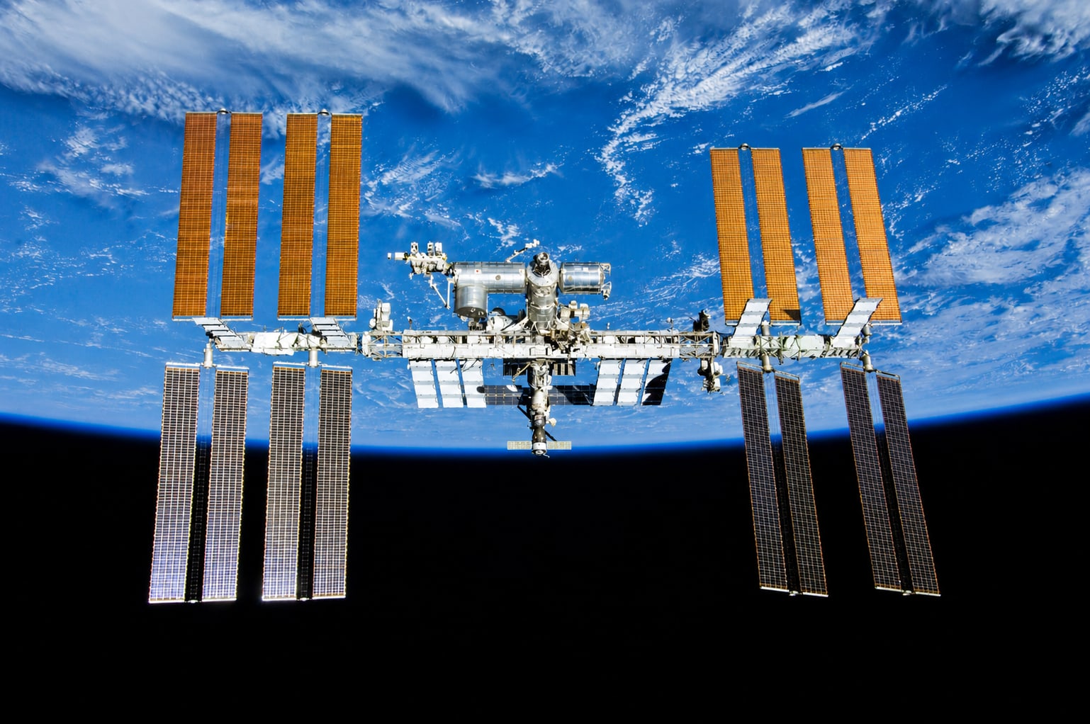 The International Space Station orbiting Earth, solar arrays extended against the planet's curvature